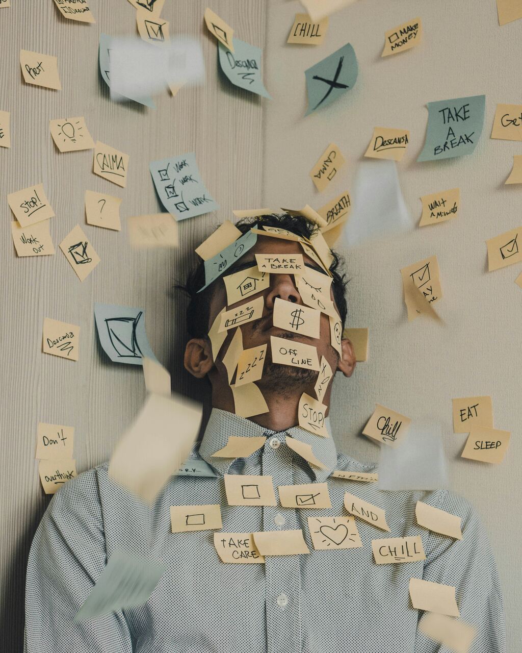 A man surrounded by falling sticky notes covered in reminders and motivational phrases, symbolizing stress and overwhelmed thoughts.